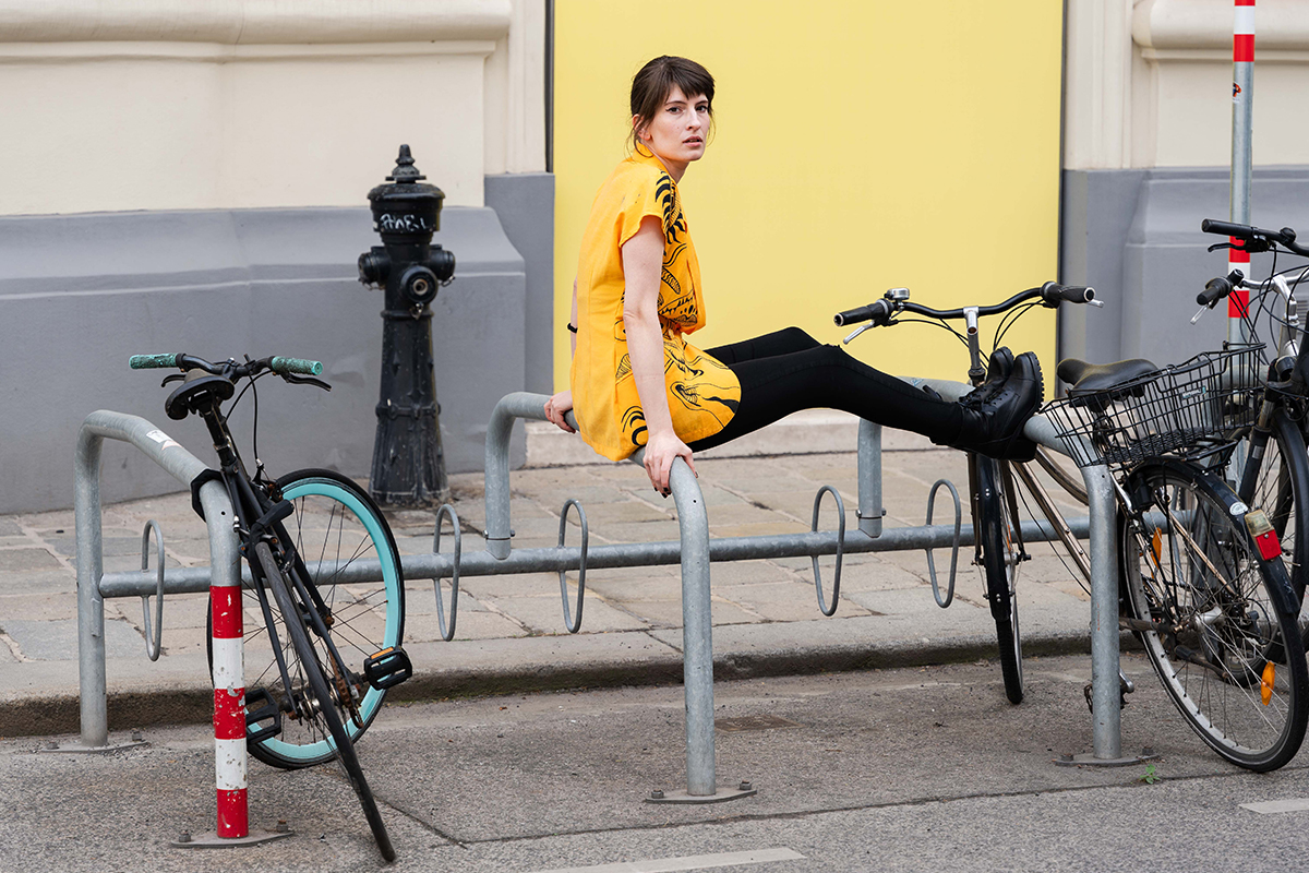 Silvia sitzt auf Fahrradständer mit bemalter gelber Bluse